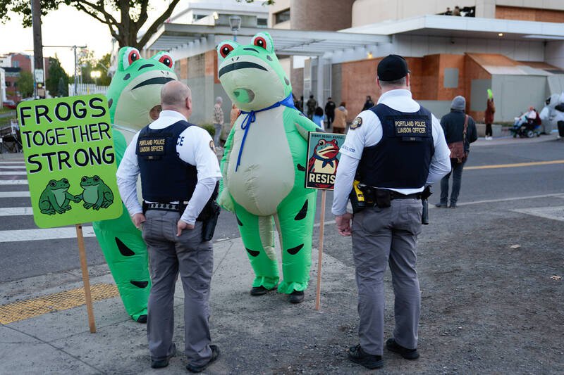 身穿充气青蛙装的抗议人士10月21日在奥勒冈州波特兰的ICE设施外与波特兰警察对话。（美联社）