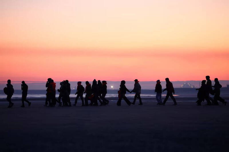 移民在黎明时分徒步走过法国北部海滩，准备搭乘小船冒险穿越英吉利海峡前往英国。正是这不断涌入的「小船移民潮」，促使英国政府拟推动史上最严苛的庇护政策改革。（路透资料照）